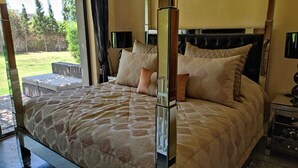 Un dormitorio con una cama grande, una mesita de noche, una lámpara y vistas al exterior.