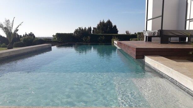 Una piscina limpia con borde de azulejos, rodeada de un jardín ajardinado y un área de estar exterior moderna.