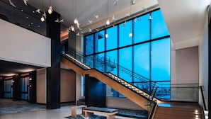 Een ruime lobby met een moderne trap, grote ramen en hangende lampen.