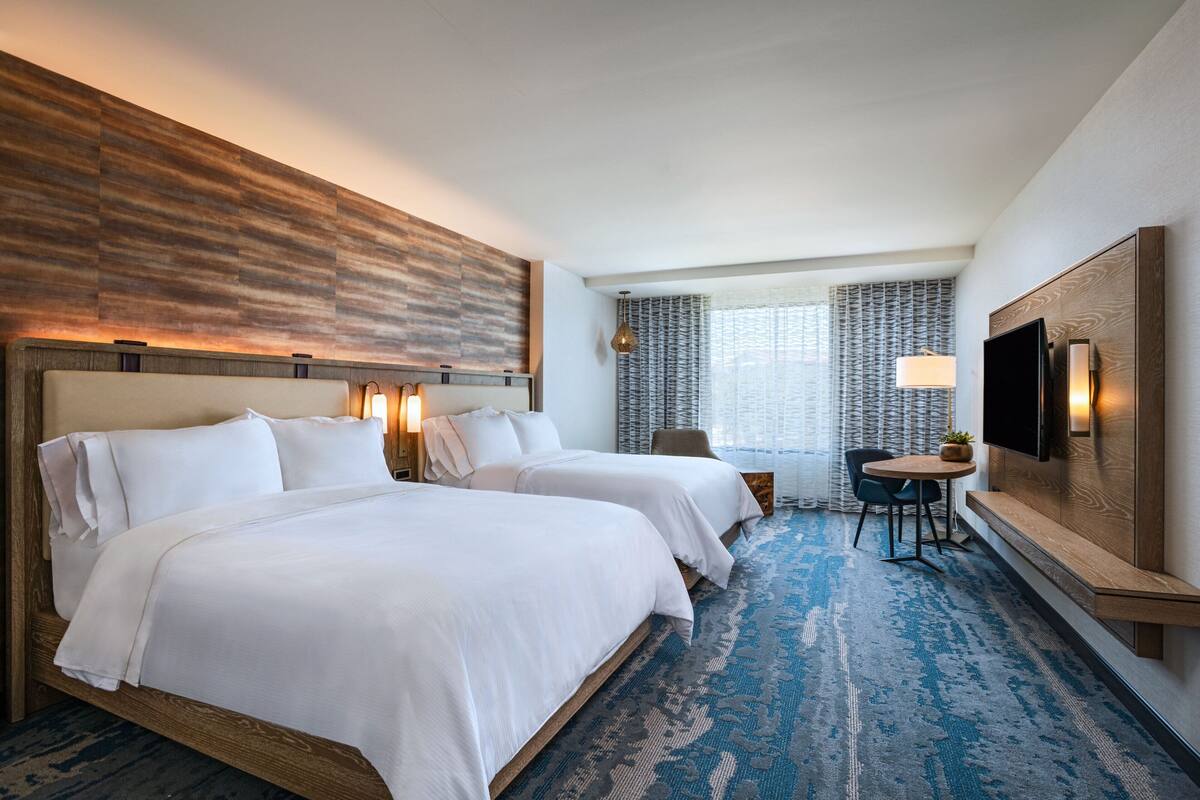Een hotelkamer met twee bedden, een televisie, een bureau en een raam met gordijnen met een patroon.