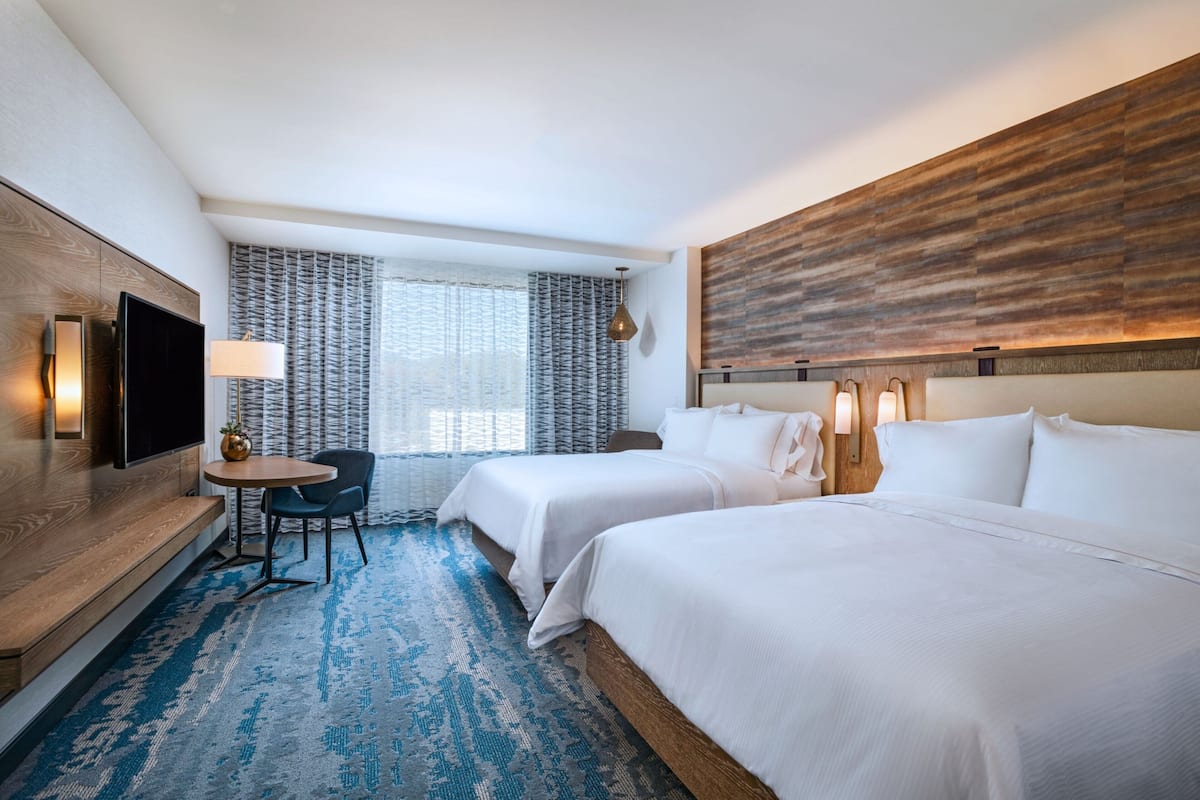Een hotelkamer met twee bedden, een televisie, een bureau met stoel en een groot raam met gordijnen.
