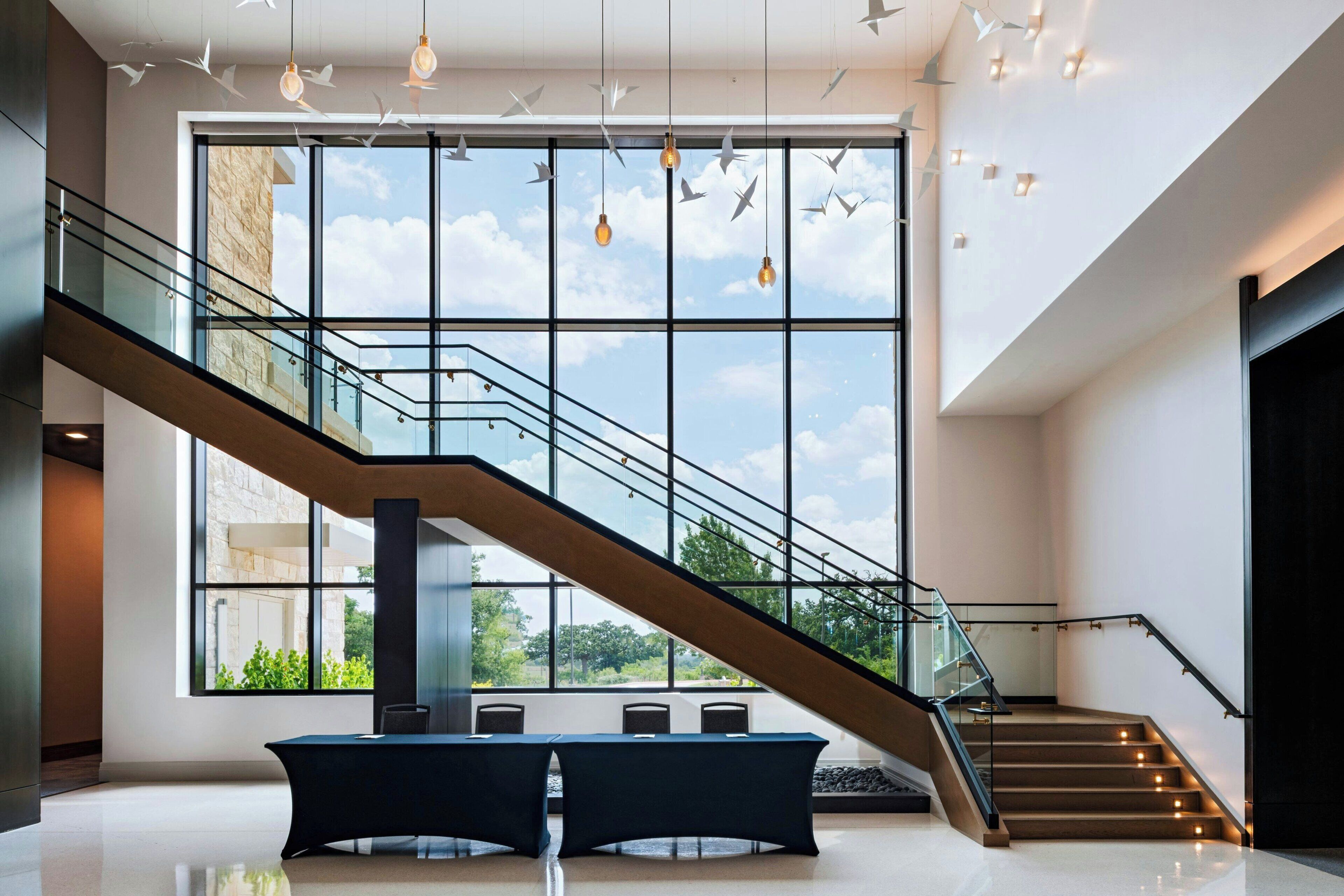 Un interior moderno con una escalera de cristal, ventanas amplias y un diseño minimalista.