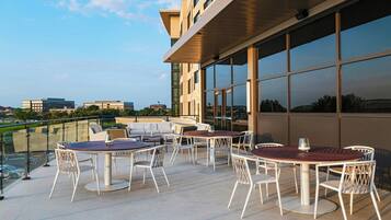 Terraço no telhado com área de estar ao ar livre e grandes janelas que oferecem vistas da paisagem urbana.
