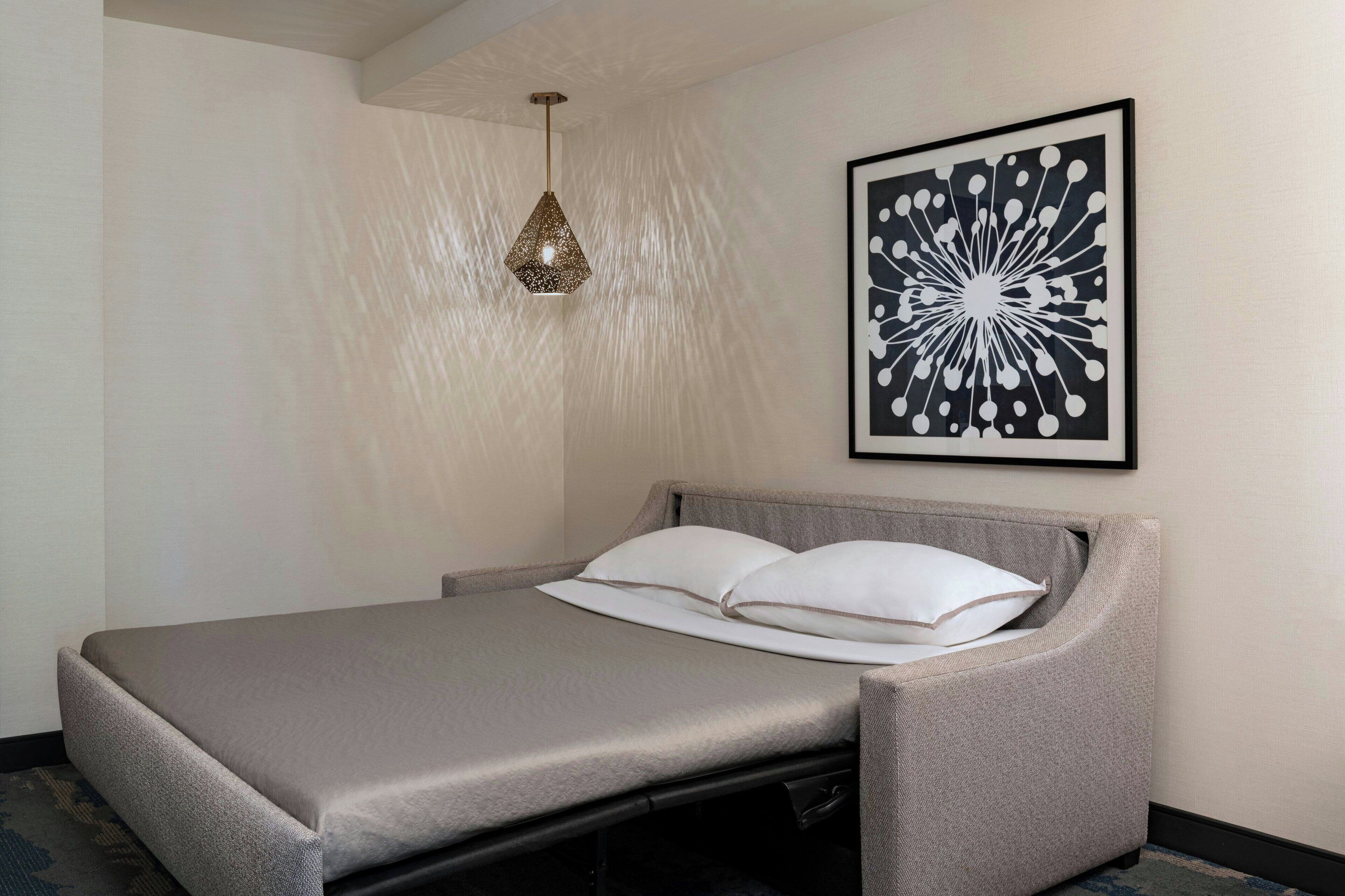 Una habitación moderna con una cama, un lámpara colgante y una obra de arte abstracto enmarcada en la pared.