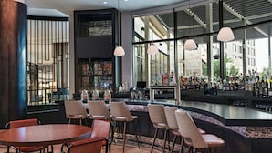 Een moderne bar met een gebogen toonbank, verschillende barkrukken en een groot raam met uitzicht op de stad.