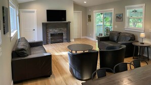 A spacious living room with a fireplace, leather sofas, a round coffee table, and a TV mounted above the fireplace. - Riverside Escape - Riverfront Home on 1 acre (Hanover Township)