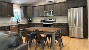 A modern kitchen with dark wood cabinets, stainless steel appliances, and a dining area with a wooden table and chairs. - Riverside Escape - Riverfront Home on 1 acre (Hanover Township)