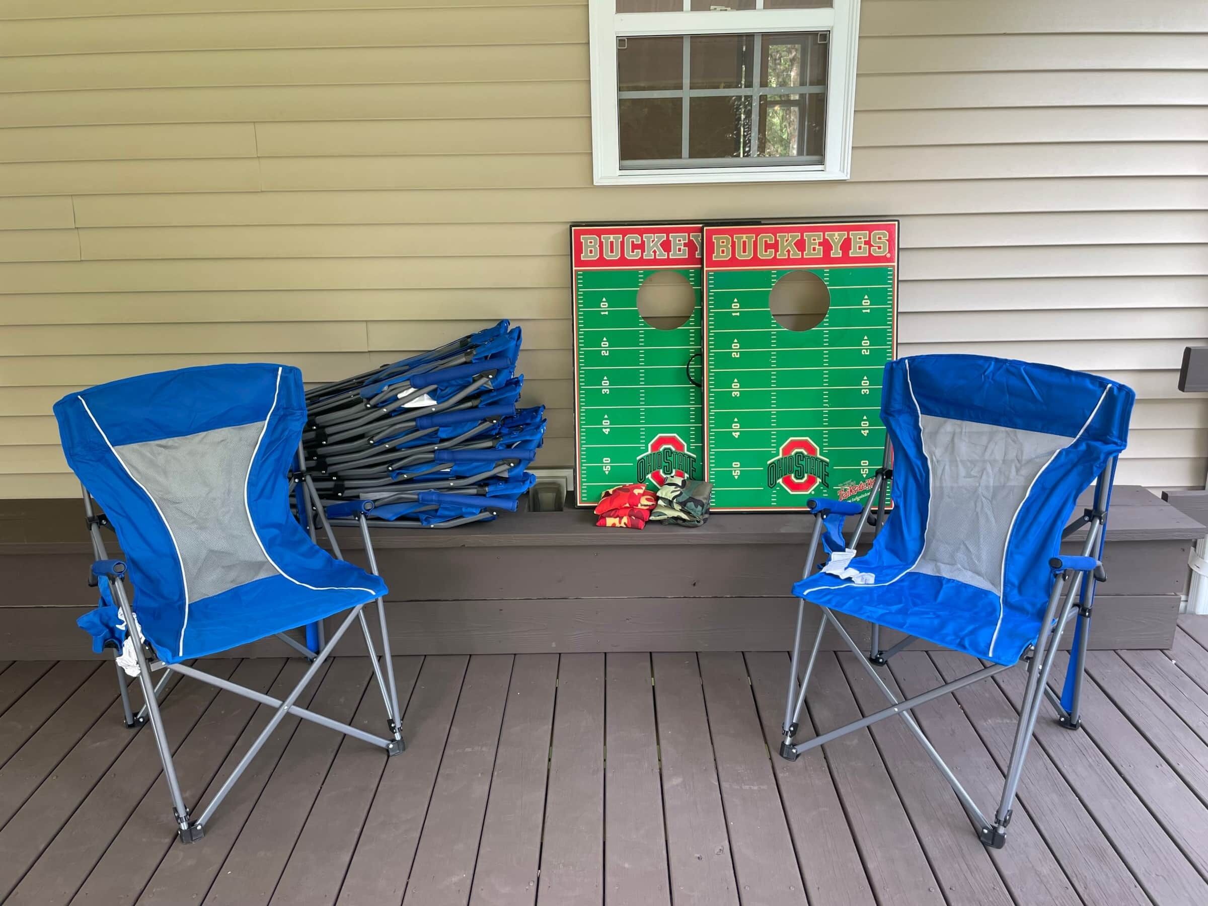Two blue folding chairs on a wooden deck with a green football-themed board game and a window above.