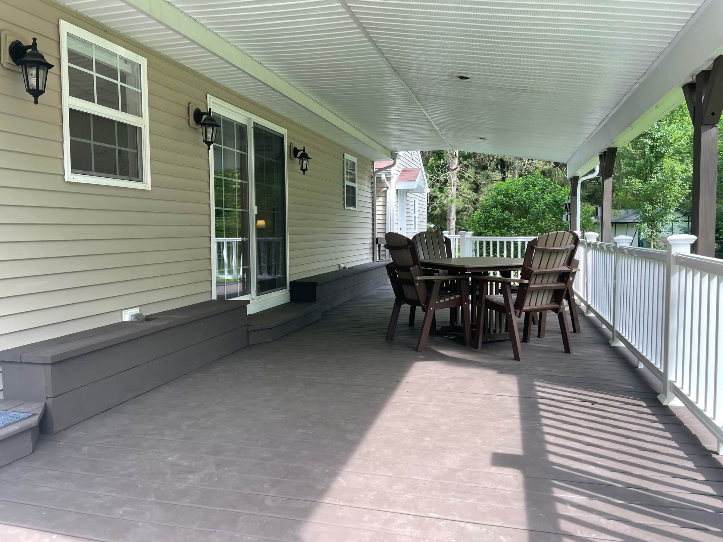 A covered porch with a table and chairs, a white railing, and a house in the background.