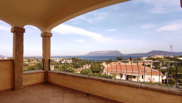 Un balcón con vista a un pueblo costero, con cielo despejado y montañas a lo lejos.