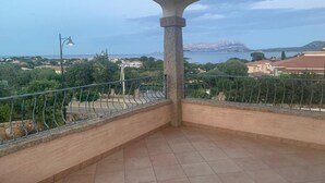 Un balcón con suelo de baldosas, barandilla metálica y vistas a un paisaje costero.