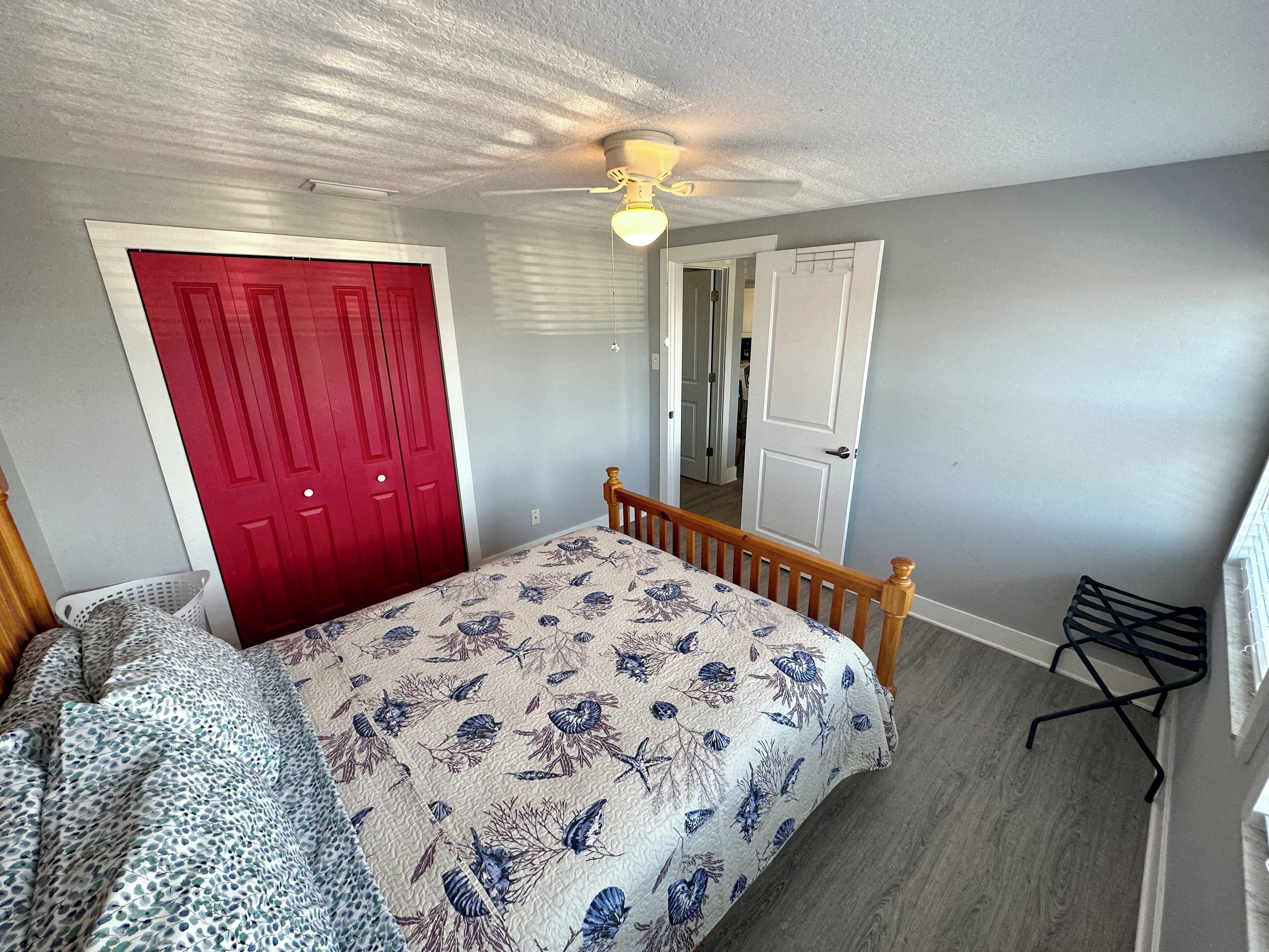 A bedroom with a bed, a red door, a white door, and a ceiling fan.