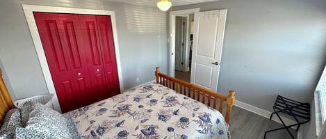 A bedroom with a bed, a red door, a white door, and a ceiling fan.