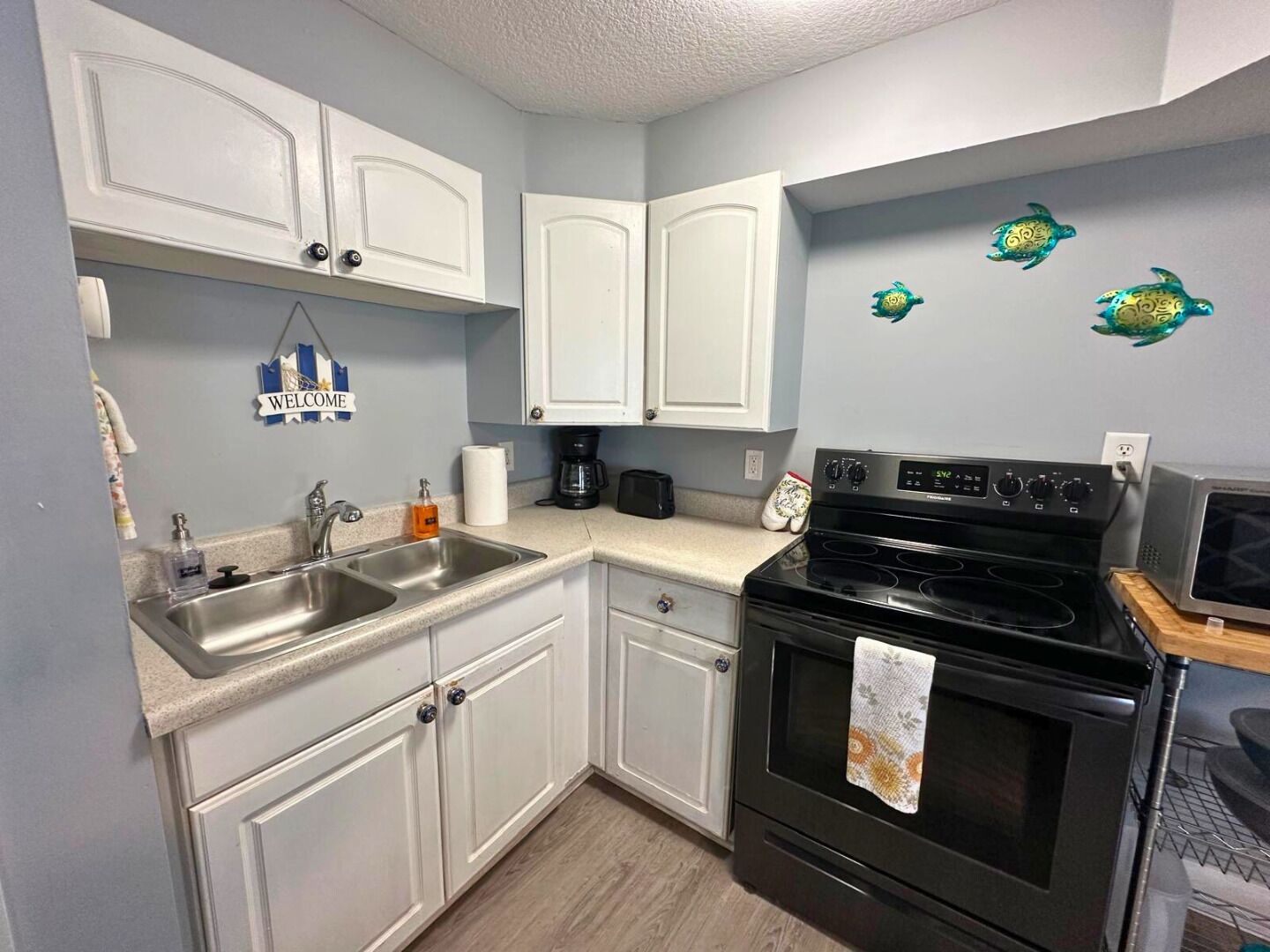 A compact kitchen with white cabinets, a black stove, and a microwave.
