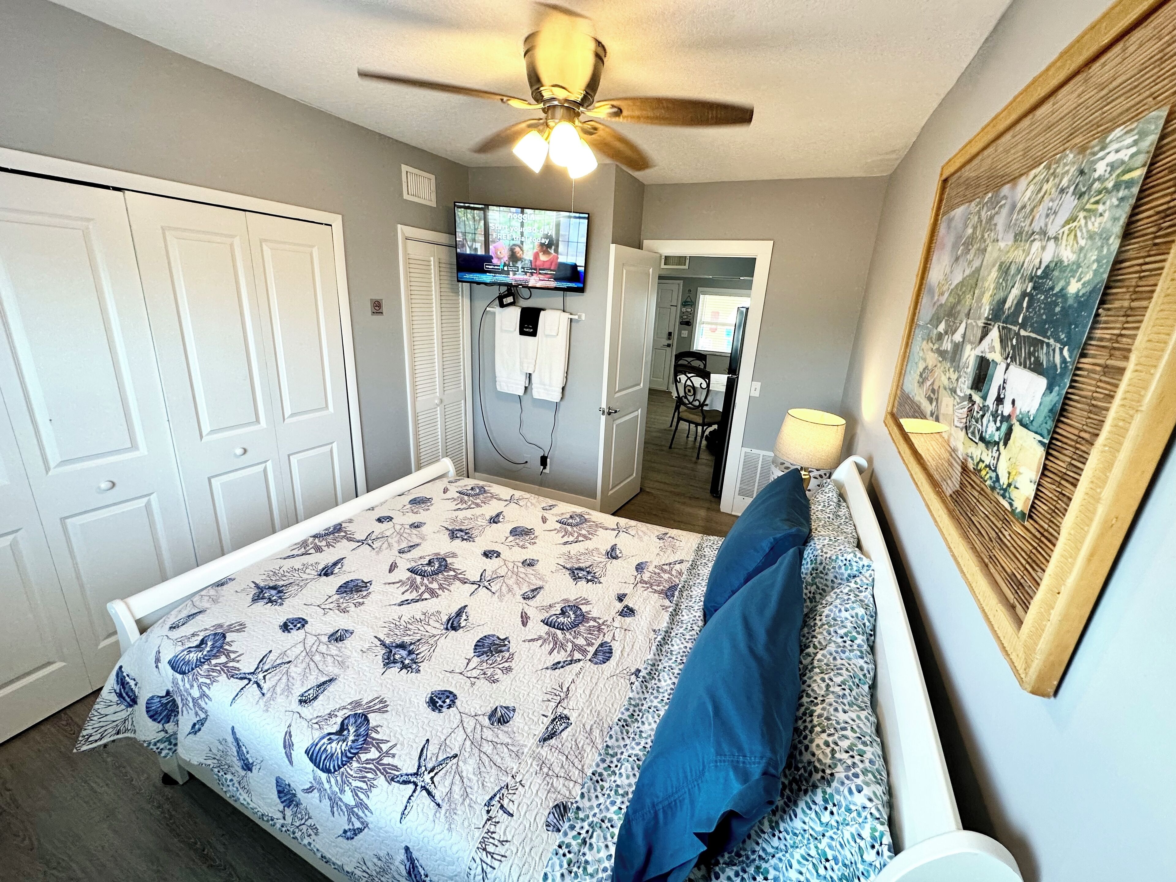 A bedroom with a bed, a ceiling fan, a TV, and a framed picture on the wall.