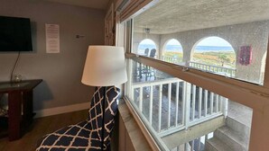 Una habitación con vistas al mar a través de ventanales abovedados, una lámpara y un televisor en la pared.