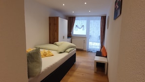 Un dormitorio con cama, una mesita, un ventanal con cortinas y un radiador.