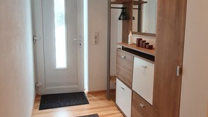 Un pasillo con suelo de madera, un tapete oscuro, un armario de madera, un espejo y una puerta con luz encima.