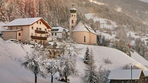Un pueblo cubierto de nieve con casas de madera tradicionales, una iglesia con campanario y montañas al fondo.