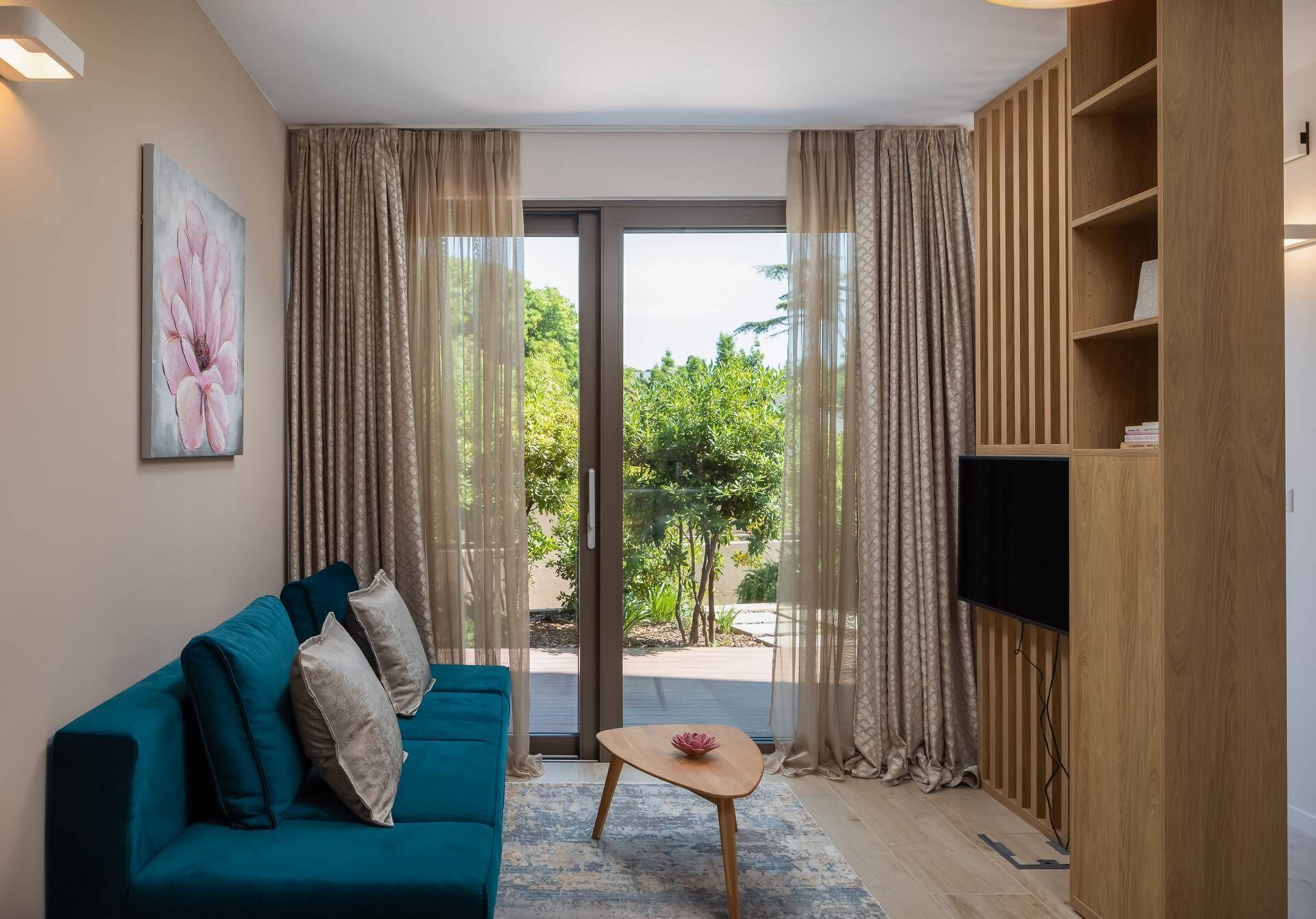 Una sala de estar con un sofá verde azulado, una mesita de madera y un televisor sobre un mueble de madera.