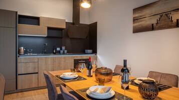 A modern kitchen with wooden cabinets, a dining table set for two, and a painting on the wall.