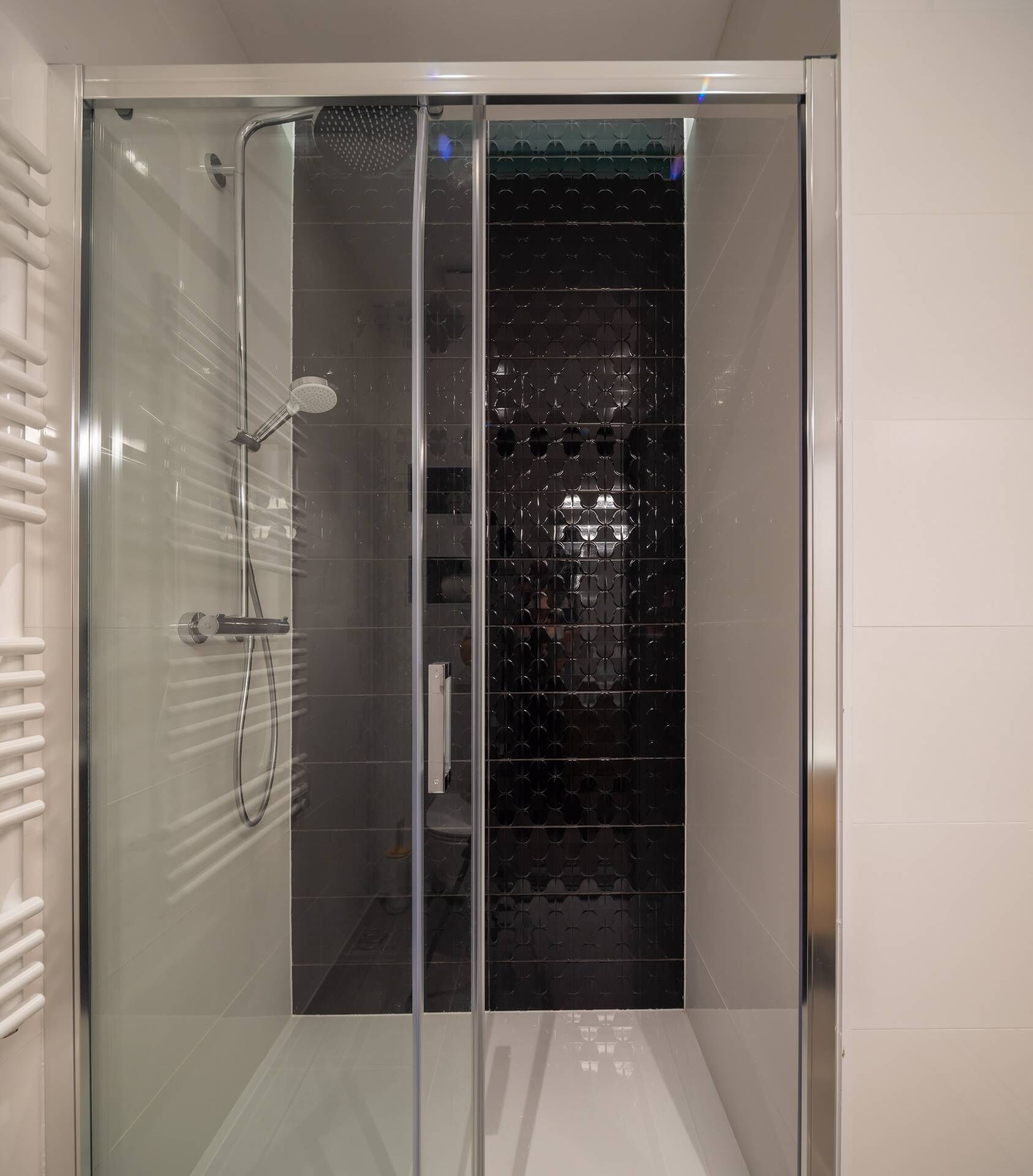 A modern shower enclosure with a glass door, a handheld showerhead, and a wall-mounted faucet.
