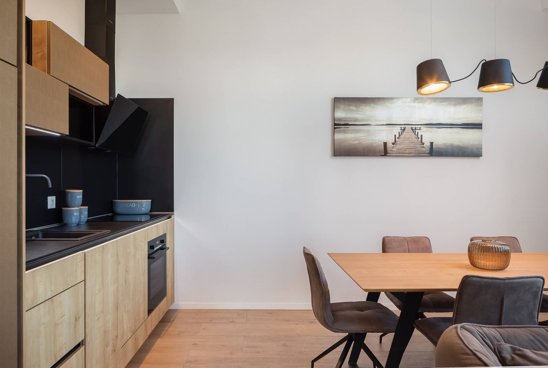 A modern kitchen with wooden cabinets, a black countertop, and a dining area with a wooden table and chairs.