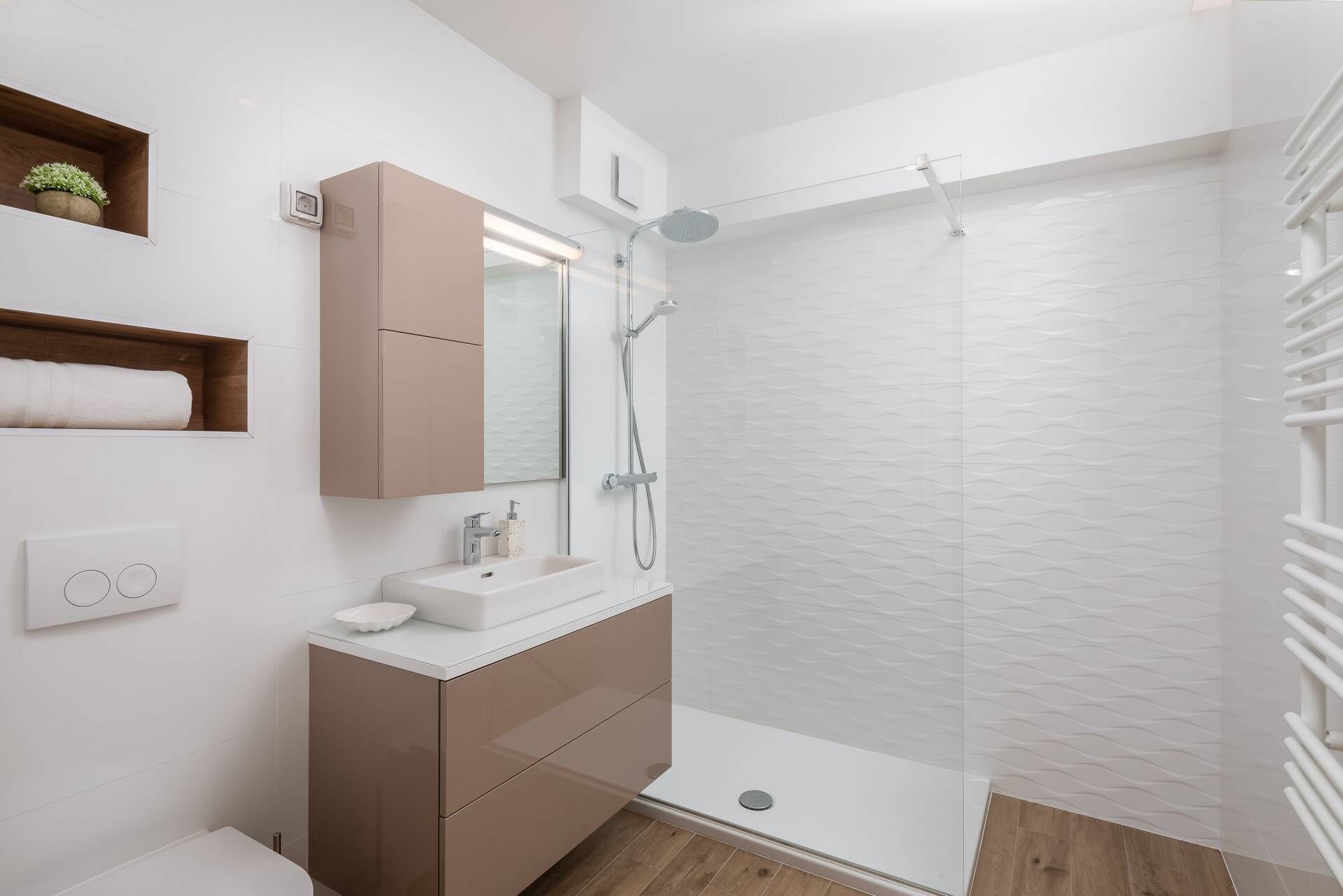 Un baño moderno con ducha envuelta en vidrio, un lavabo blanco y un mueble de tocador de madera.
