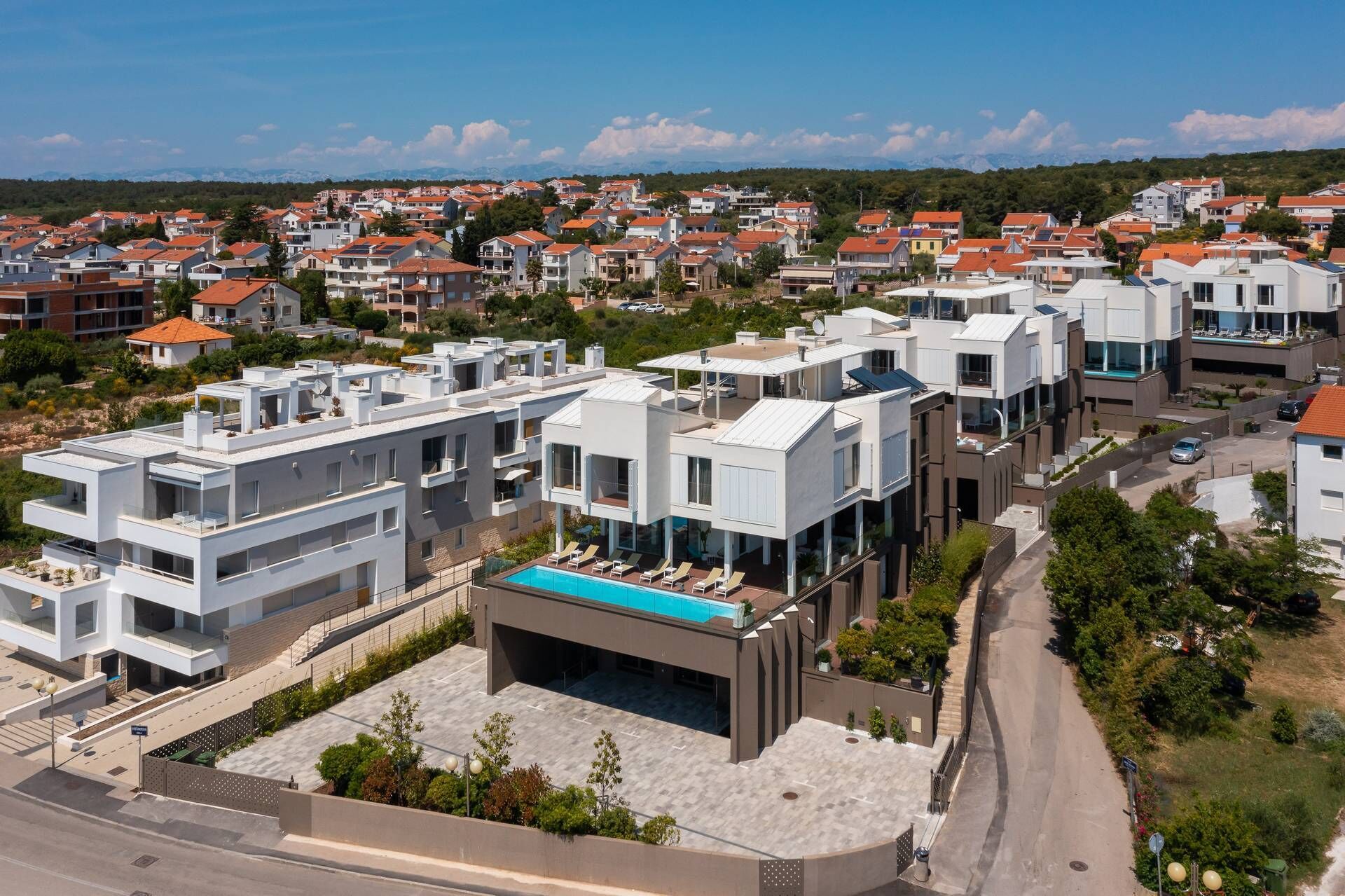 A modern residential area with contemporary architecture, featuring a prominent building with a rooftop pool and a spacious courtyard.