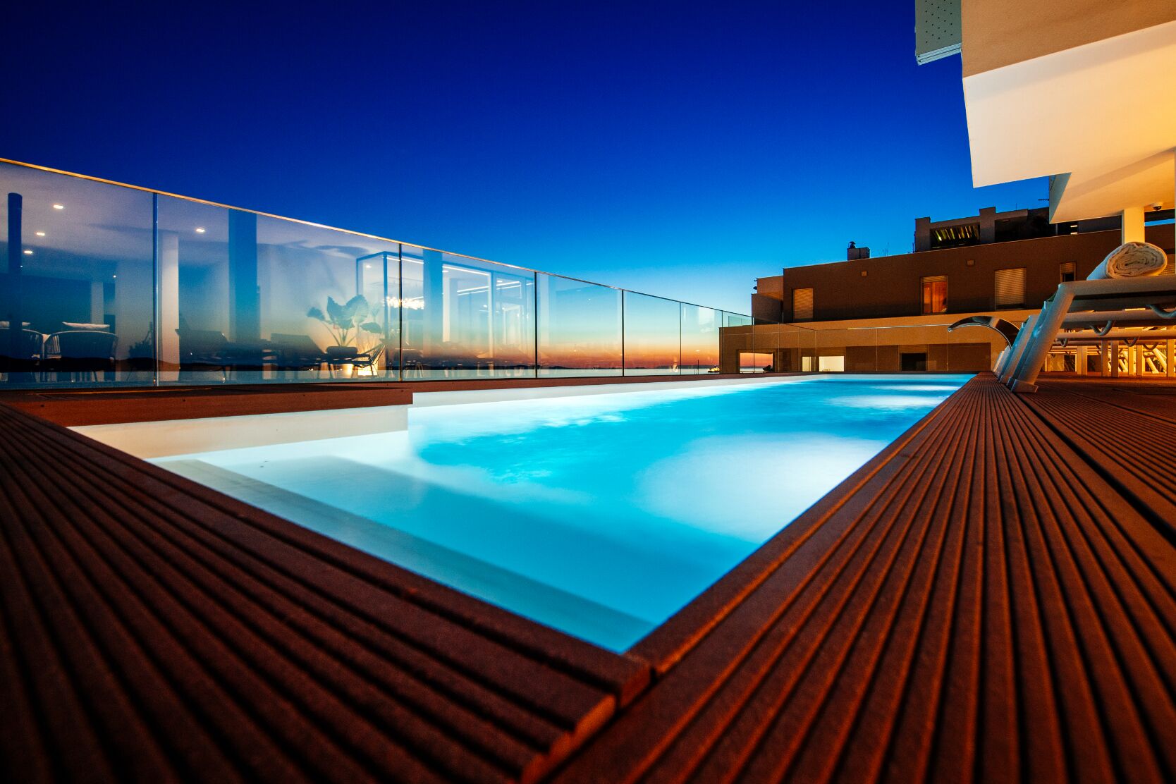 A rooftop pool with glass railings and a wooden deck.