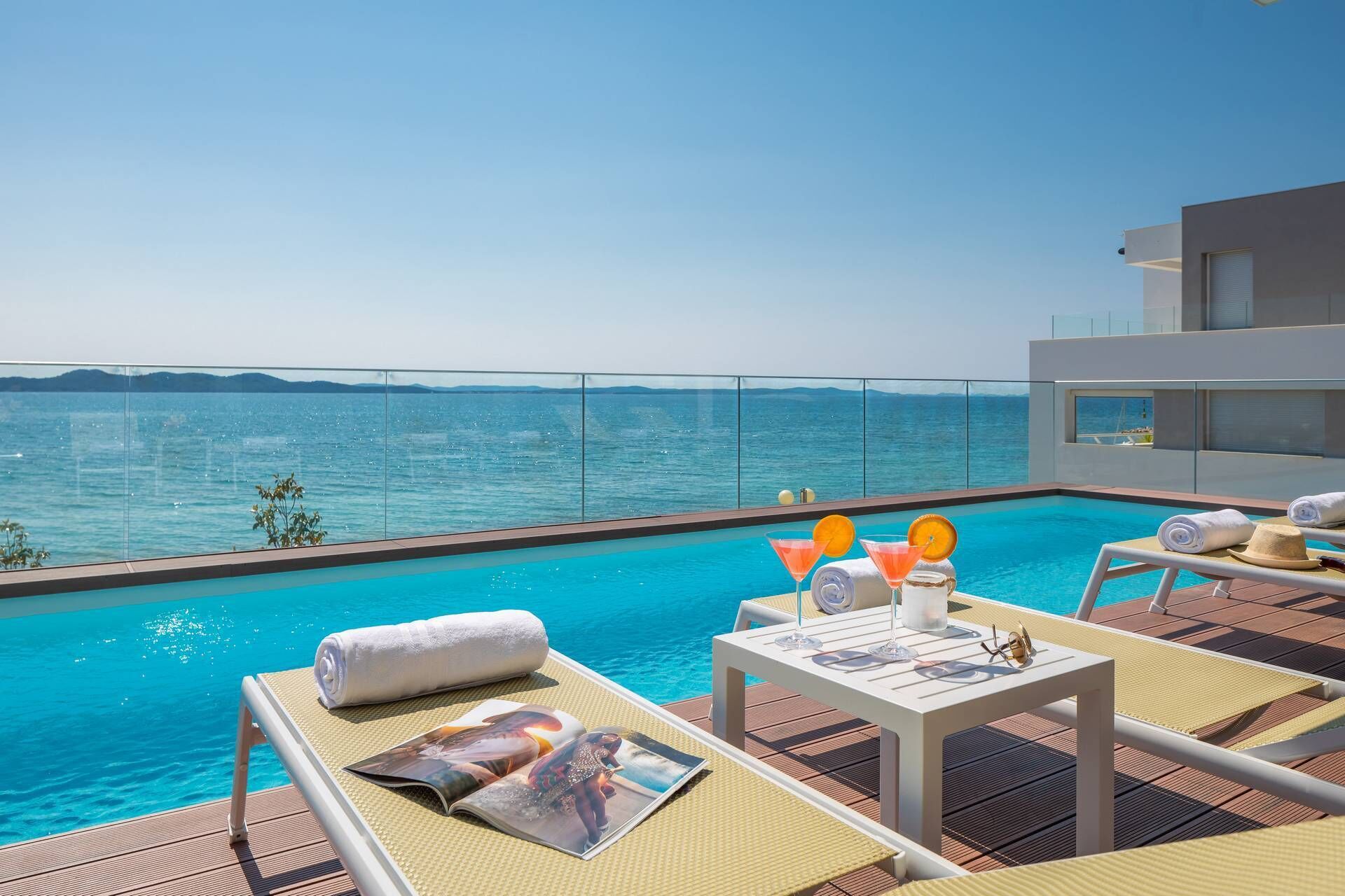 Un espace aménagé au bord de la piscine, avec des chaises longues, une table où sont servis des boissons et une vue sur la mer.