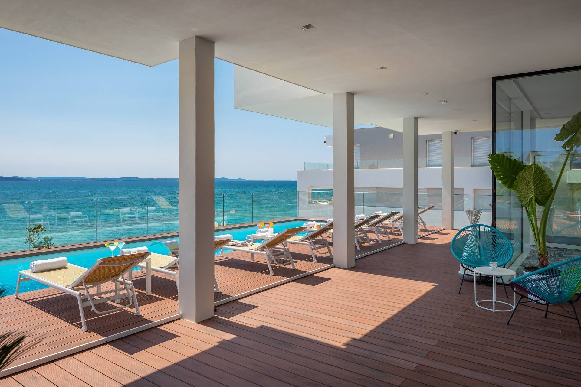 A modern outdoor deck with a pool, lounge chairs, and a view of the sea.