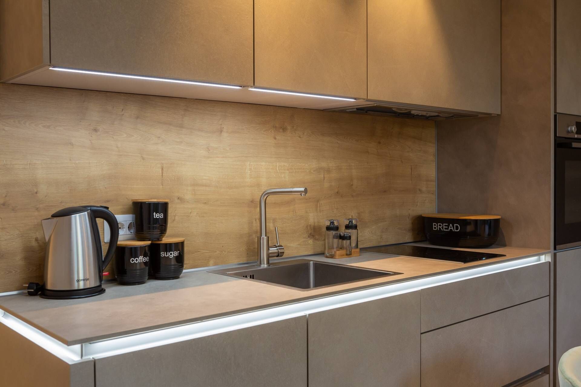Una cocina moderna con un lavamanos de acero inoxidable, una cafetera, recipientes para azúcar y café, un panera y un horno empotrado.