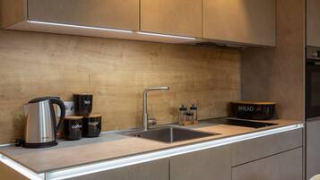 Una cocina moderna con un lavamanos de acero inoxidable, una cafetera, recipientes para azúcar y café, un panera y un horno empotrado.