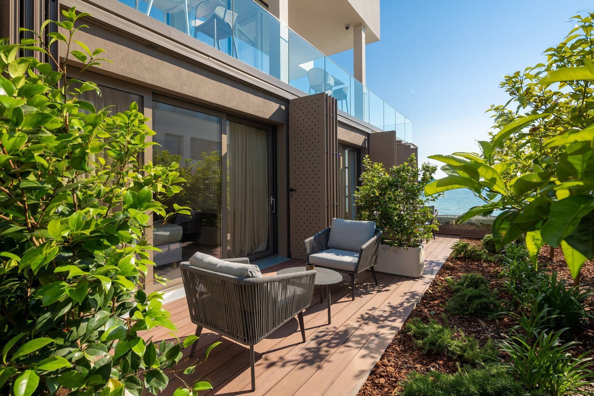 Une terrasse extérieure moderne, dotée d’un espace salon, d’une porte vitrée donnant sur un balcon et offrant une vue sur la mer.