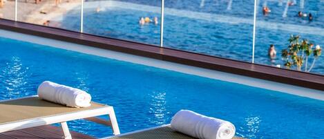 A poolside area with lounge chairs and a view of a busy beach and water activities.