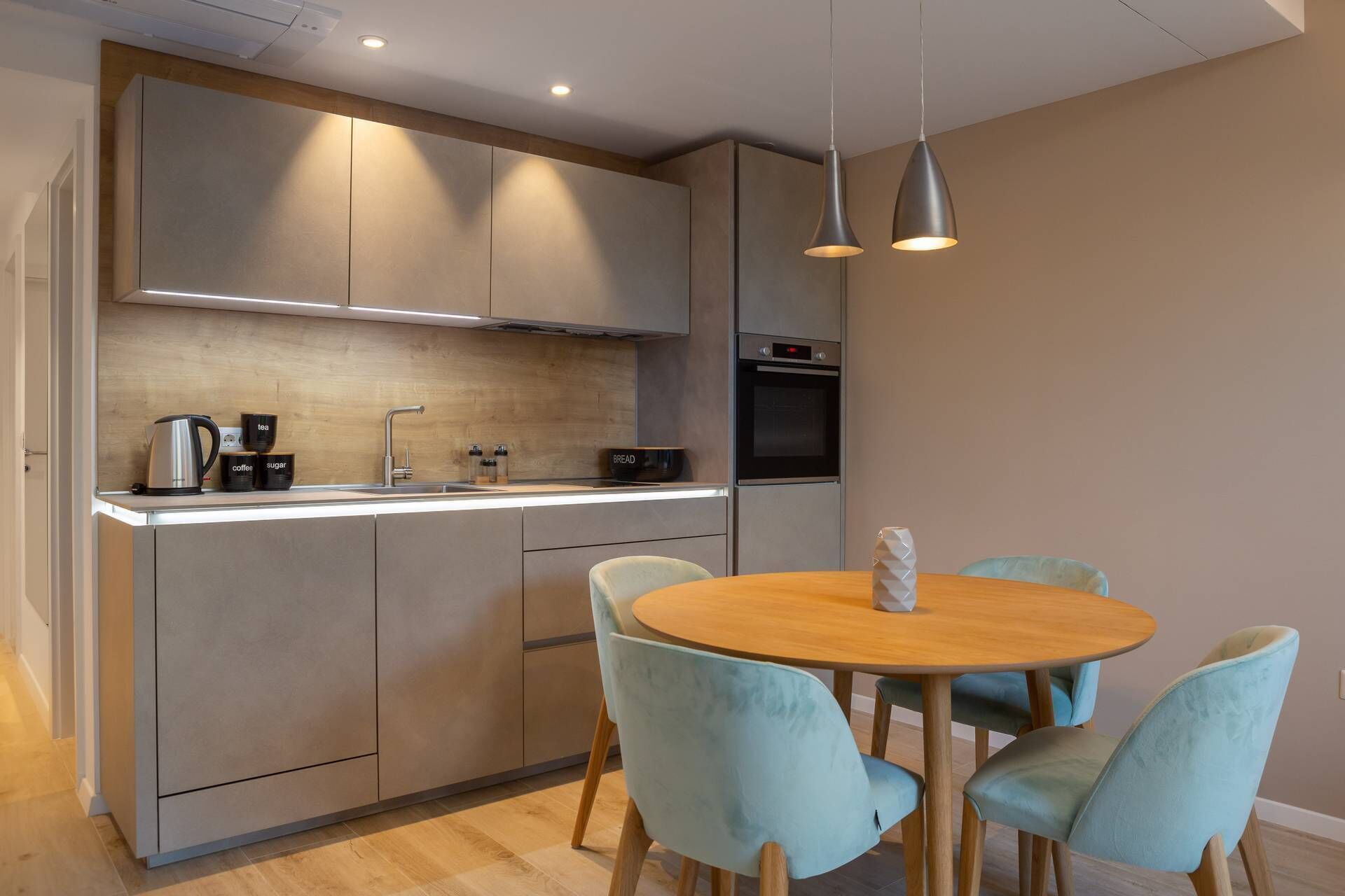 Une cuisine moderne dotée d’un îlot central, d’appareils électroménagers intégrés et de chaises bleu clair recouvertes de tissu, disposées autour d’une table en bois.