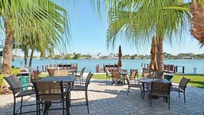 Un patio al aire libre con mesas y sillas, palmeras y vista al agua.