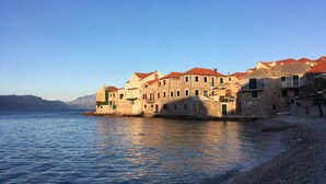 Complejo de edificios costeros con arquitectura de piedra y techos de tejas rojas, frente a un mar tranquilo.
