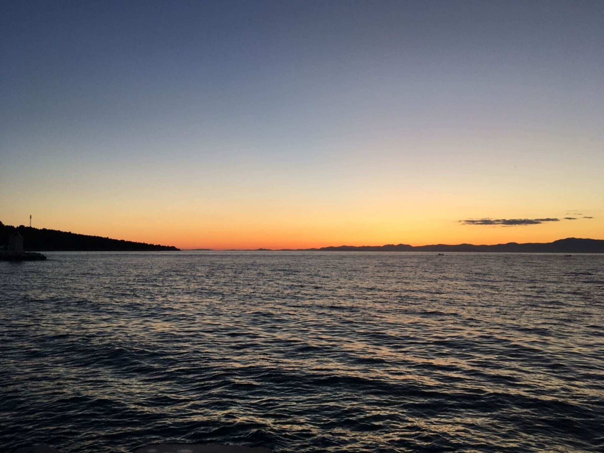 A calm body of water with a distant shoreline silhouette during sunset.