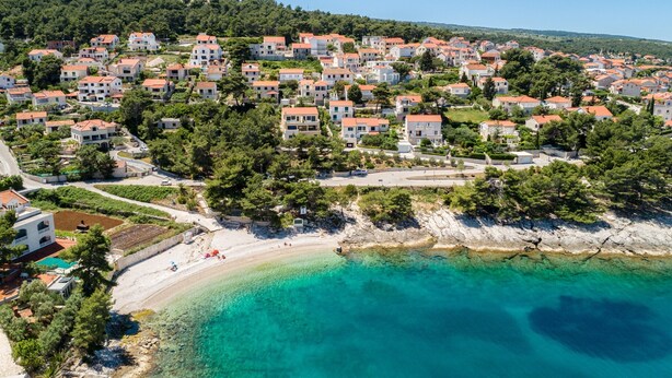 Vista aérea de una zona residencial costera con casas, una playa y aguas turquesas cristalinas.