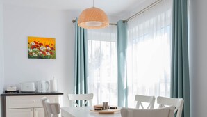 Uma área de refeições com uma mesa e cadeiras brancas, um lustre e uma janela com cortinas.