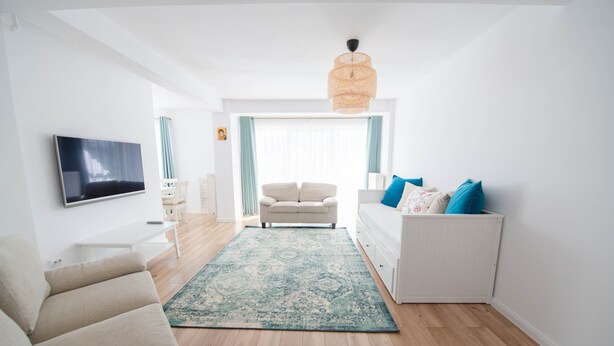 Uma sala de estar moderna com sofá, mesa de centro, televisão e uma grande janela com cortinas.