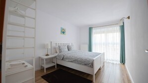 Quarto com cama, mesas de cabeceira, guarda-roupa e janela com cortinas.