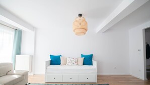 Uma sala de estar moderna com um sofá branco, almofadas azuis, um tapete estampado e uma luminária pendente de fibra natural.