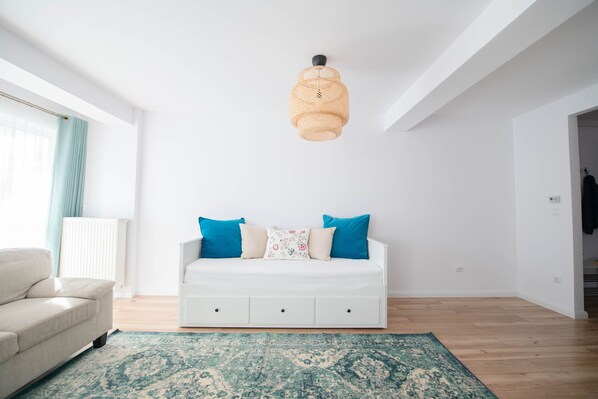 A modern living room with a white sofa, blue cushions, a patterned rug, and a woven pendant light.