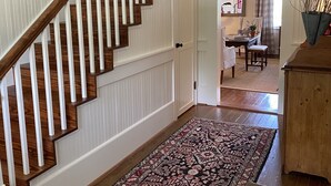 A staircase with wooden steps and white railings, leading to a room with a patterned rug and a wooden cabinet. - Farm House Inn - Quiet Country Elegance (New Ulm)