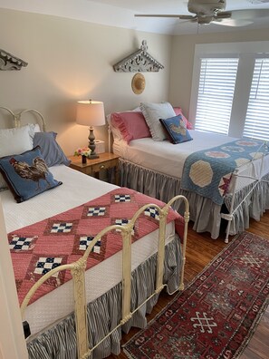 A bedroom with two beds, a ceiling fan, a decorative wall hanging, and a window with blinds. - Farm House Inn - Quiet Country Elegance (New Ulm)