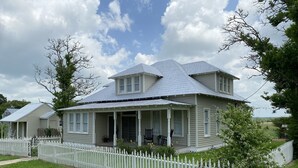 A two-story house with a porch, a white picket fence, and a grassy yard. - Farm House Inn - Quiet Country Elegance (New Ulm)
