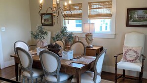 A dining room with a chandelier, wooden chairs, a table with a placemat, and a window with blinds. - Farm House Inn - Quiet Country Elegance (New Ulm)